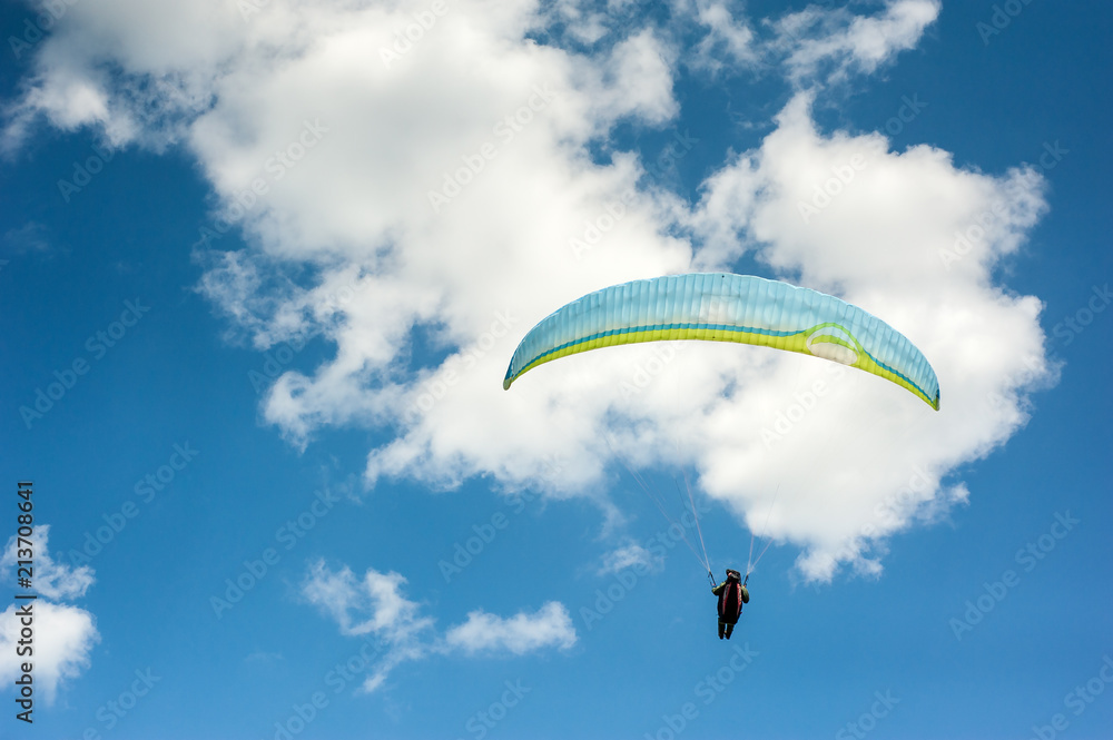 Paraglider flying in the blue sky against the background of clouds. Paragliding in the sky on a sunny day. Paraglider flying in the blue sky against the background of clouds. Paragliding in the sky on a sunny day.