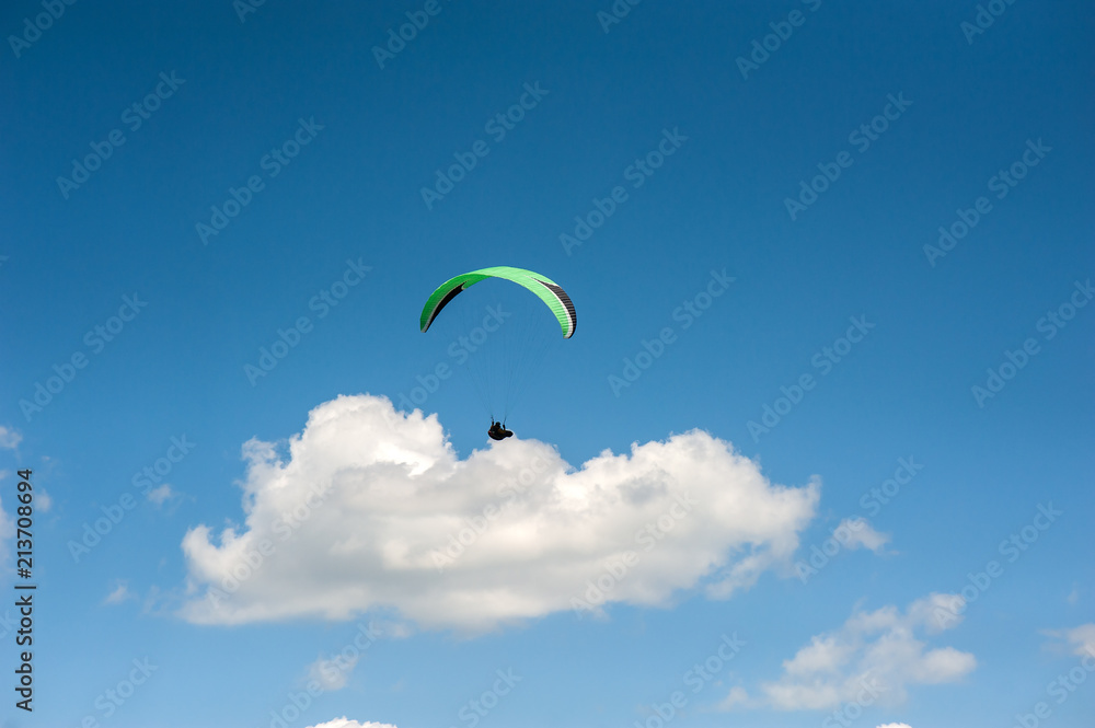 Paraglider flying in the blue sky against the background of clouds. Paragliding in the sky on a sunny day. Paraglider flying in the blue sky against the background of clouds. Paragliding in the sky on a sunny day.