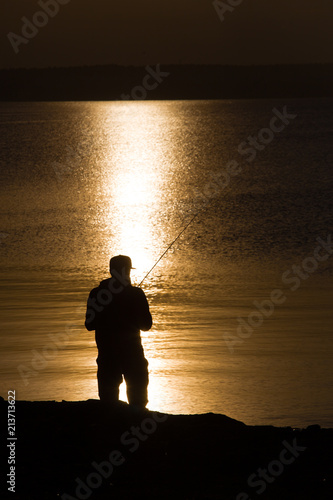 Silhouette of fisherman with fishing rod on the shore of pond