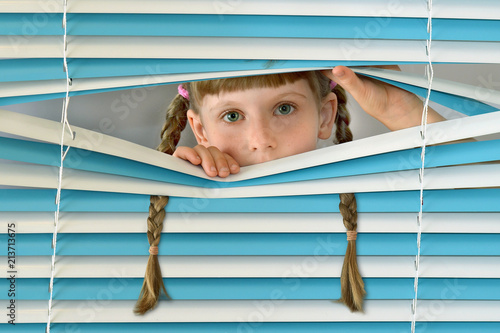 child, kid looks out the window through the blinds