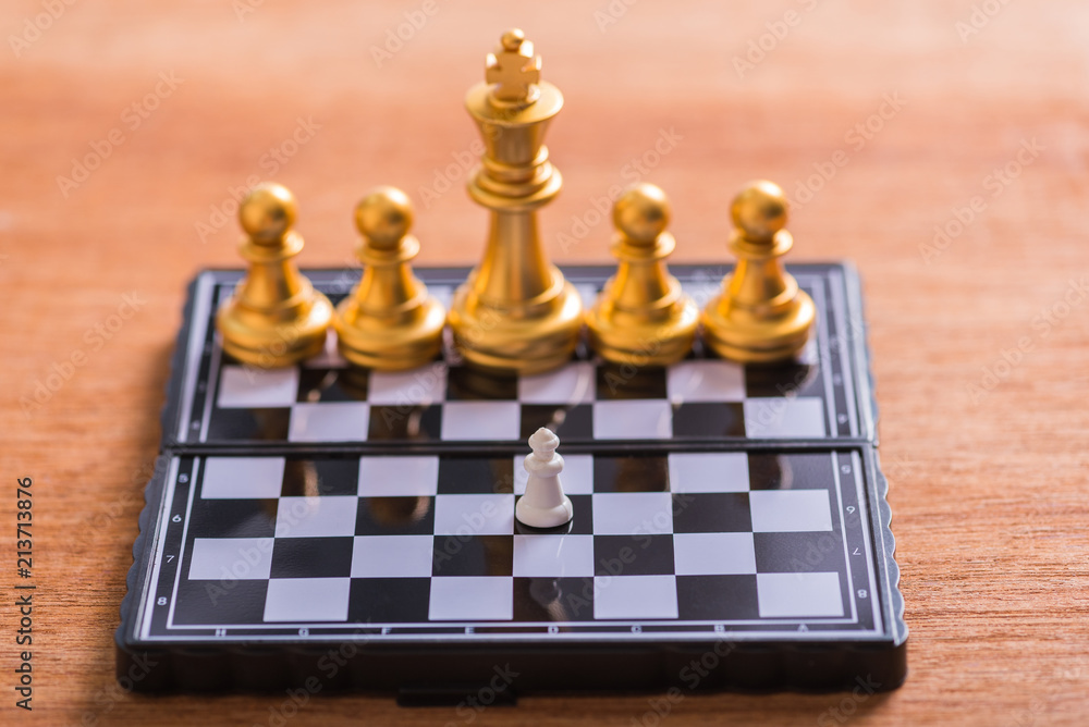a small white chess pieces against very big gold chess team on board a small white chess pieces against very big gold chess team on board