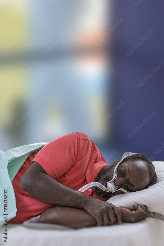 Exhausted afro-american man with sleep apnea using CPAP machine, wearing headgear mask connecting to air tube Exhausted afro-american man with sleep apnea using CPAP machine, wearing headgear mask connecting to air tube