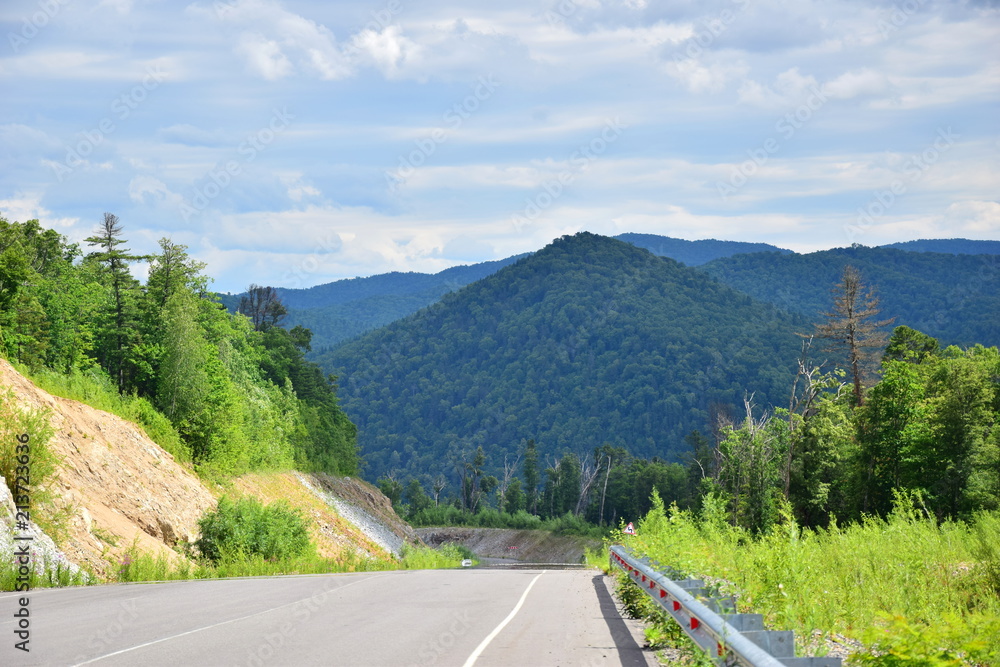 Asphalt road in the hills. Among the green mountains is a road. Around green hills, dense forest, blue sky. Russian far East. The mountains of Sikhote-Alin.