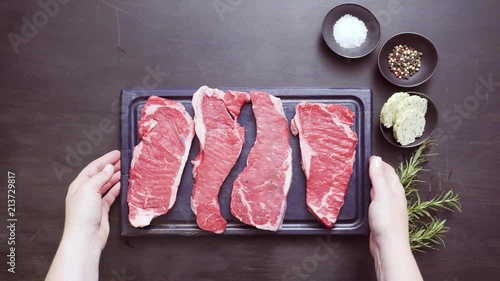 Raw New York strip steaks with fresh rosemary and herb butter on a wood cutting board photo