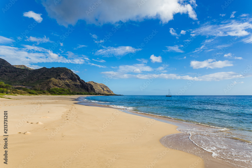 Makua beach view with beatiful mountains and a sailboat in the background, Oahu island, Hawaii