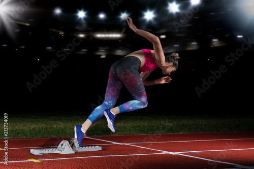 woman sprinter leaving starting blocks on the athletic track. exploding start on stadium with reflectors