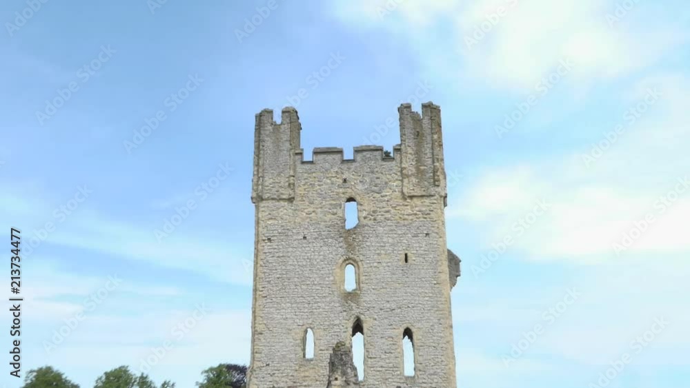 Zoom out shot of a medieval tower in ruins on a blue sky with grassy ground Zoom out shot of a medieval tower in ruins on a blue sky with grassy ground