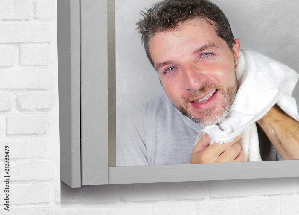 Fototapeta premium young happy attractive man using towel drying face after washing looking at the bathroom mirror smiling cheerful and positive feeling clean and fresh