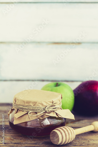 Rosh HaShanah or a Jewish New Year with copy space including two apples and a glass jar of honey on vintage or rustic wooden table background