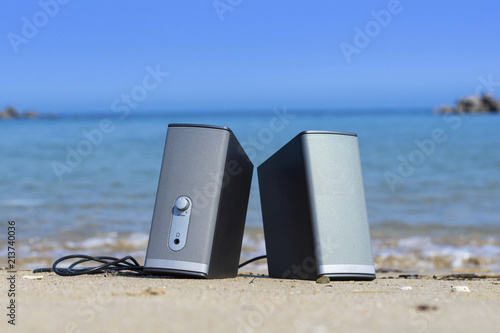 A pair of speakers on the beach with blue sea water in the background ready for beach party on a sunny day. 