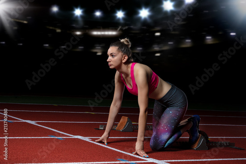 woman sprinter leaving starting blocks on the athletic track. exploding start on stadium with reflectors
