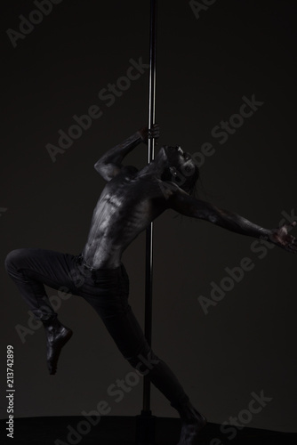 Pole dance sport. Muscular man with silver body art dancing on pylon. macho with metal skin. dancer workout on pole. Freedom. Training her flexibility. Athletic man make acrobatic elements on pylon