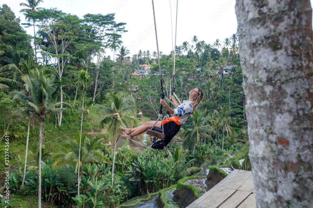 Young tourist woman swinging on the cliff in the jungle rainforest of a tropical Bali island, Indonesia