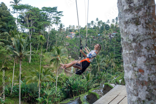 Young tourist woman swinging on the cliff in the jungle rainforest of a tropical Bali island, Indonesia