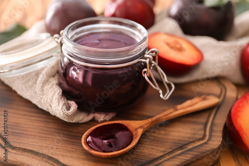 Jar with tasty plum jam on wooden board
