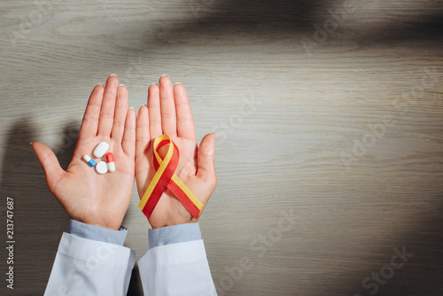 partial view of female doctor holding ribbon and pills, world hepatitis day concept