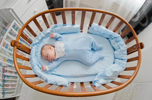 Baby's restful sleep. Newborn baby in a wooden crib. The baby sleeps in the bedside cradle. Safe living together in a bedside cot. The little boy dozed off under a knitted blanket.