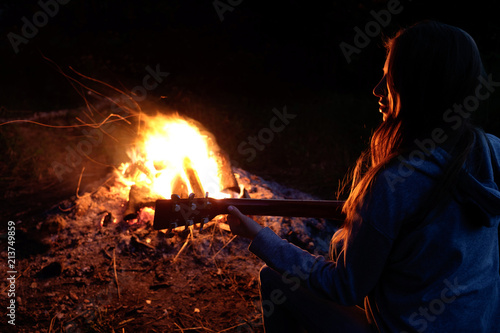 Young redhead woman playing guitar near bonfire at night camp
