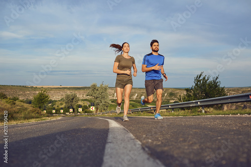 A guy and a girl jog along the road in nature. The couple is running.