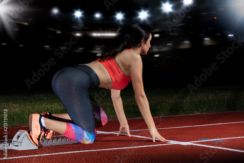 woman sprinter leaving starting blocks on the athletic track. exploding start on stadium with reflectors