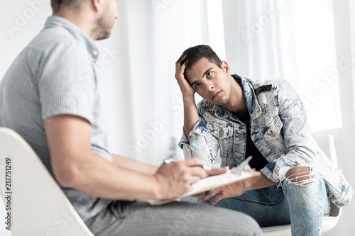 Rebellious spanish man listening to counsellor during therapy for youth