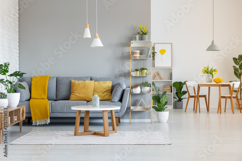 Lamps above wooden table in open space interior with yellow blanket on grey sofa. Real photo photo