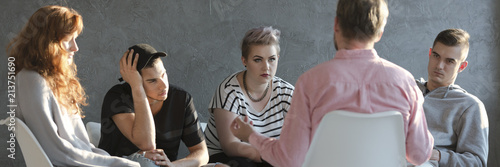 Difficult teenagers listening to psychotherapist during meeting of support group photo