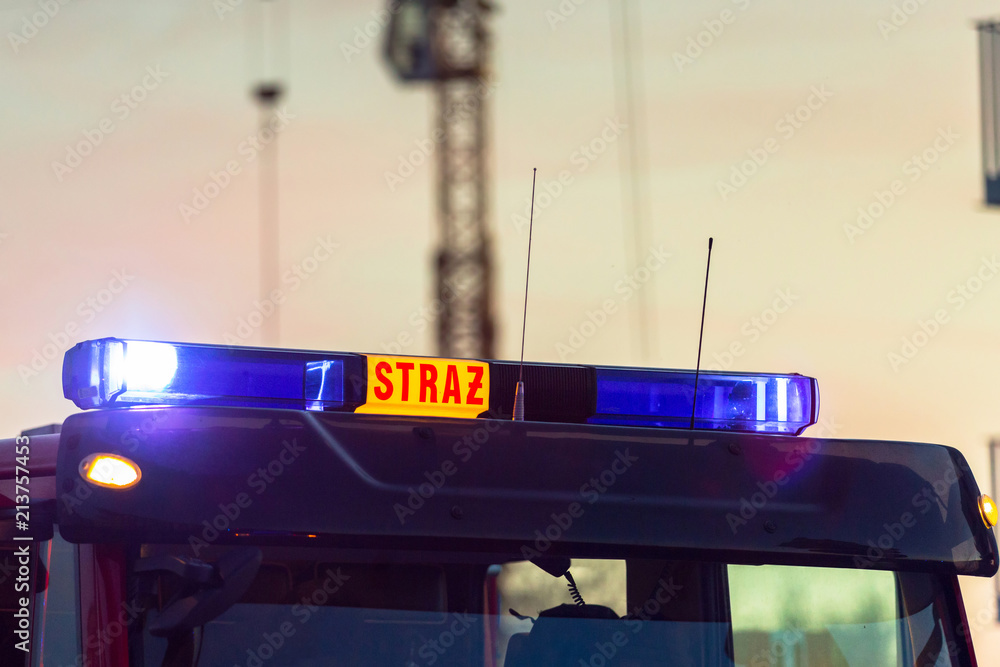 Fototapeta premium Flashing lights of red fire truck in Poland (Straz) at dusk