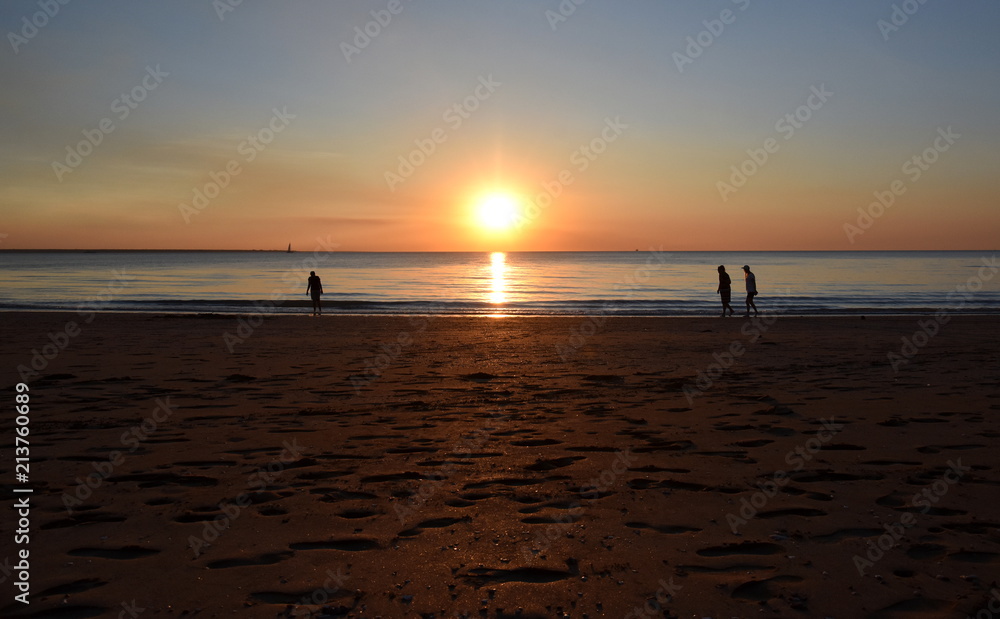 People enjoy the sunset at Mindil Beach. The Sun casts orange shades across an evening sky at Mindil Beach (Darwin, Northern Territory, Australia).