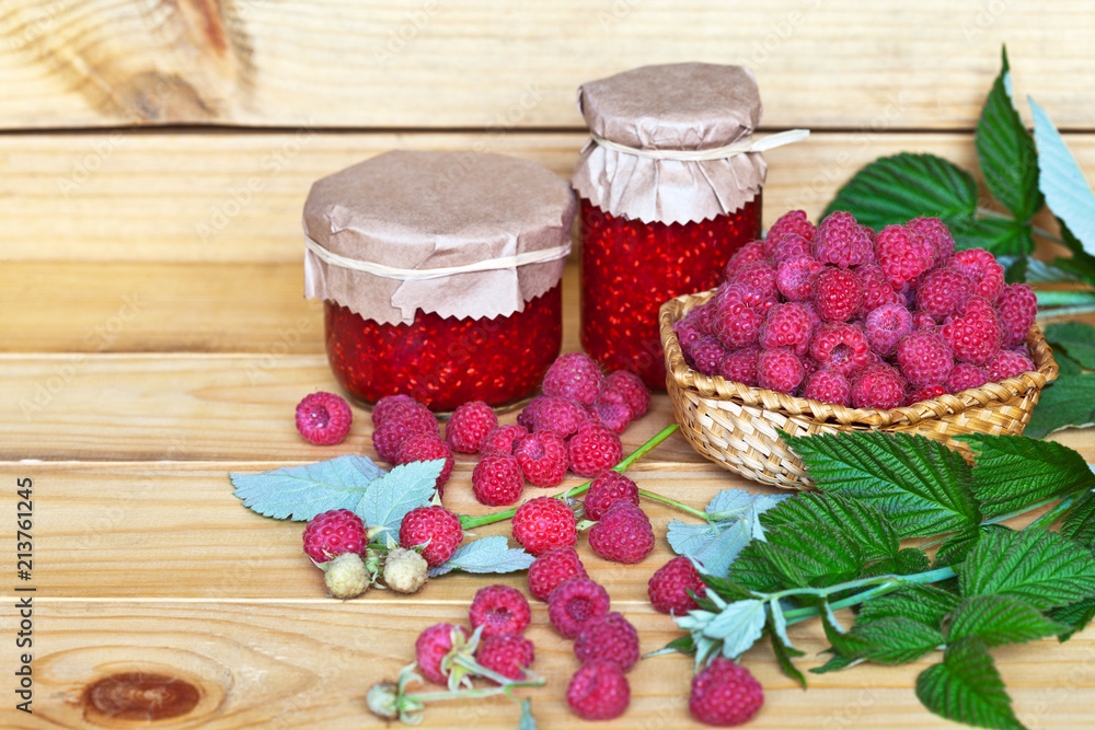 Fresh ripe garden raspberry in a wicker bowl and homemade jam on a wooden background. Rustic still life. Close-up view. Place for text Fresh ripe garden raspberry in a wicker bowl and homemade jam on a wooden background. Rustic still life. Close-up view. Place for text