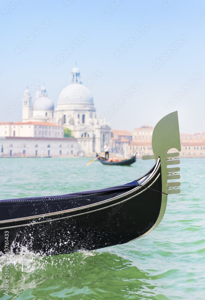 Traditional venetian gondola and gondolier with tourists between Grand Canal and Giudecca Canal of Venice city against basilica Santa Maria della Salute background. Italy.