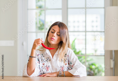 Young woman at home eating red hot chili pepper with a confident expression on smart face thinking serious