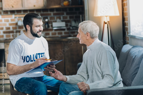 Conducting a poll. Charming content dark-haired volunteer smiling and talking with an aged man and conducting a poll