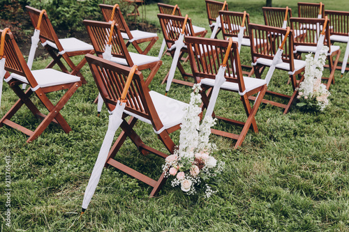 In area of wedding ceremony on the green grass in the park are chairs for guests