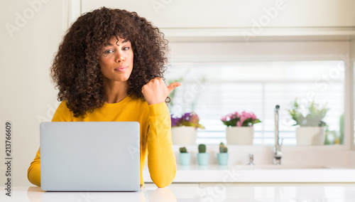 African american woman using computer laptop at kitchen pointing with hand and finger up with happy face smiling
