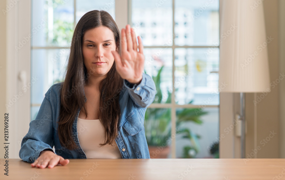 Young beautiful woman at home with open hand doing stop sign with serious and confident expression, defense gesture Young beautiful woman at home with open hand doing stop sign with serious and confident expression, defense gesture