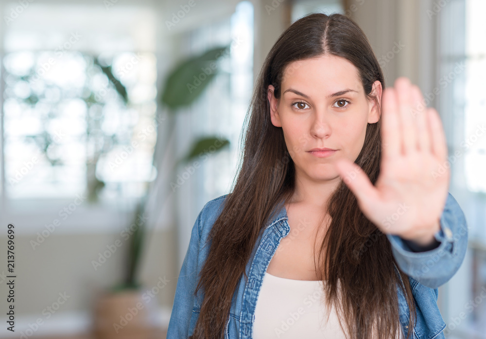 Young beautiful woman at home with open hand doing stop sign with serious and confident expression, defense gesture