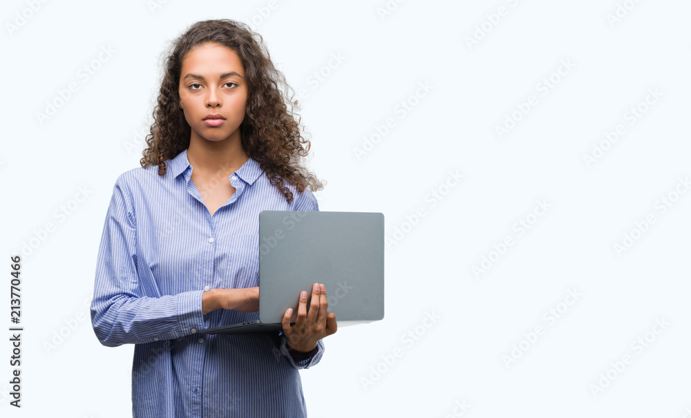 Young hispanic woman holding computer laptop with a confident expression on smart face thinking serious Young hispanic woman holding computer laptop with a confident expression on smart face thinking serious