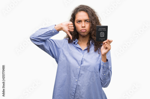 Young hispanic woman holding passport of Italy with angry face, negative sign showing dislike with thumbs down, rejection concept