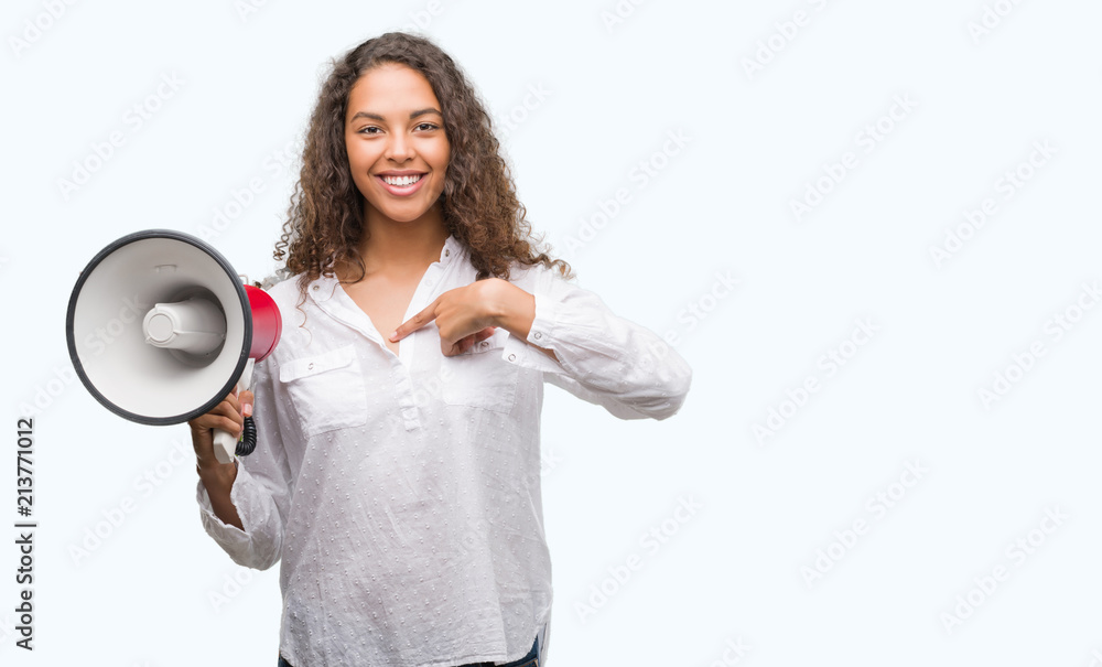 Young hispanic woman holding megaphone with surprise face pointing finger to himself Young hispanic woman holding megaphone with surprise face pointing finger to himself