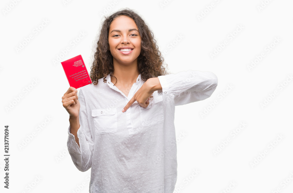 Young hispanic woman holding passport of Switzerland with surprise face pointing finger to himself Young hispanic woman holding passport of Switzerland with surprise face pointing finger to himself