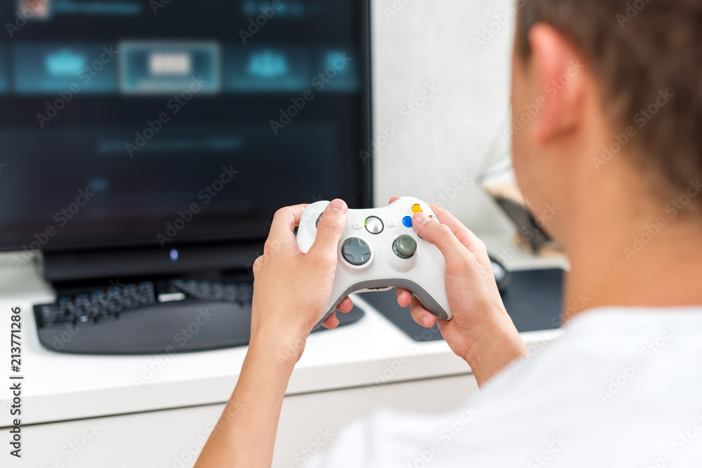 Happy young man playing and winning online game on computer. Back view of  gamer with video console gamepad controller. Competitive gaming, electronic  sports, technology, gaming, entertainment concept. Stock Photo