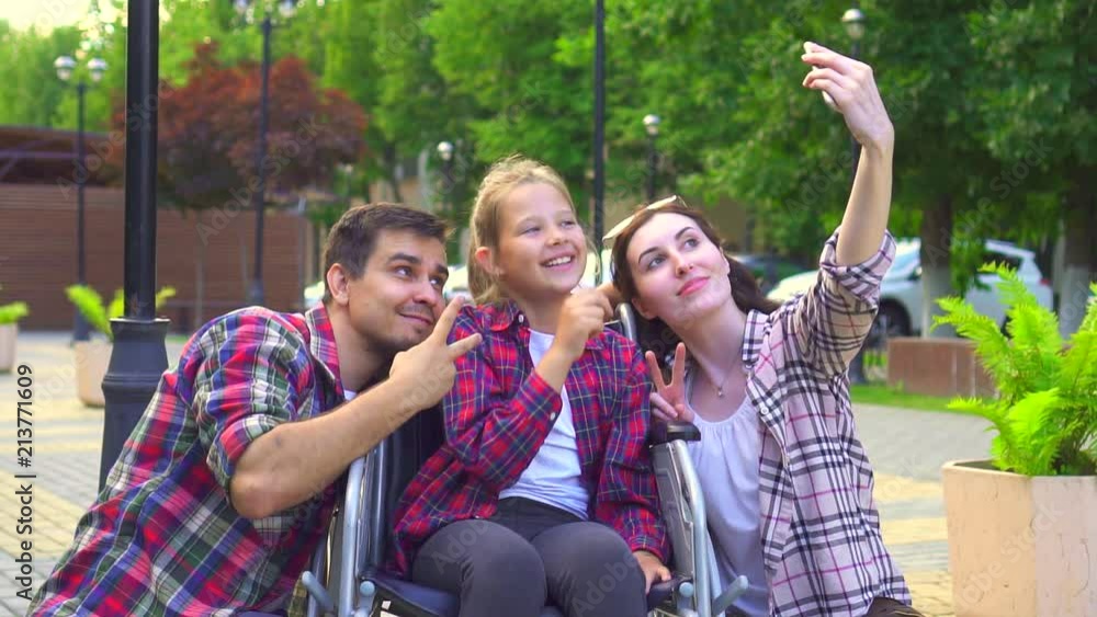 portrait of mom and dad with a little disabled daughter in a wheelchair doing a selfie portrait of mom and dad with a little disabled daughter in a wheelchair doing a selfie