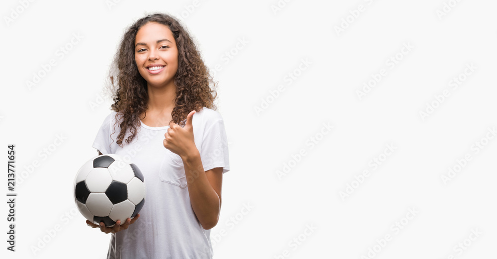 Young hispanic woman holding soccer football ball happy with big smile doing ok sign, thumb up with fingers, excellent sign