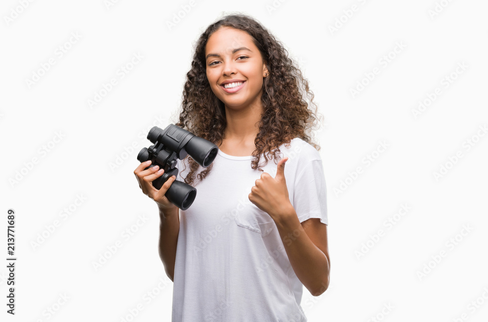 Young hispanic woman looking through binoculars happy with big smile doing ok sign, thumb up with fingers, excellent sign Young hispanic woman looking through binoculars happy with big smile doing ok sign, thumb up with fingers, excellent sign