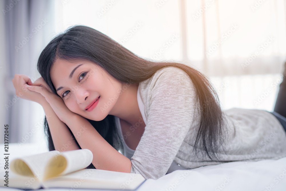 Pretty attractive Asian woman reading a fiction book, laying on the bed at bedroom 