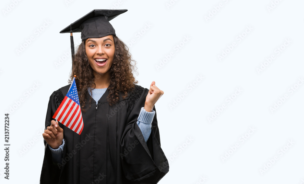 Young hispanic woman wearing graduation uniform holding flag of United States screaming proud and celebrating victory and success very excited, cheering emotion Young hispanic woman wearing graduation uniform holding flag of United States screaming proud and celebrating victory and success very excited, cheering emotion