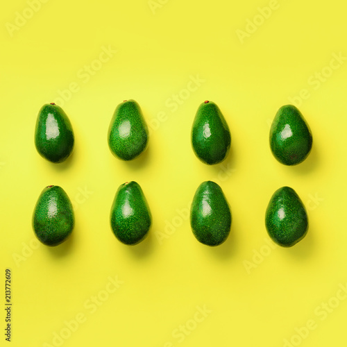 Green avocado pattern on yellow background. Square crop. Top view. Pop art design, creative summer food concept. Organic avocadoes in minimal flat lay style.