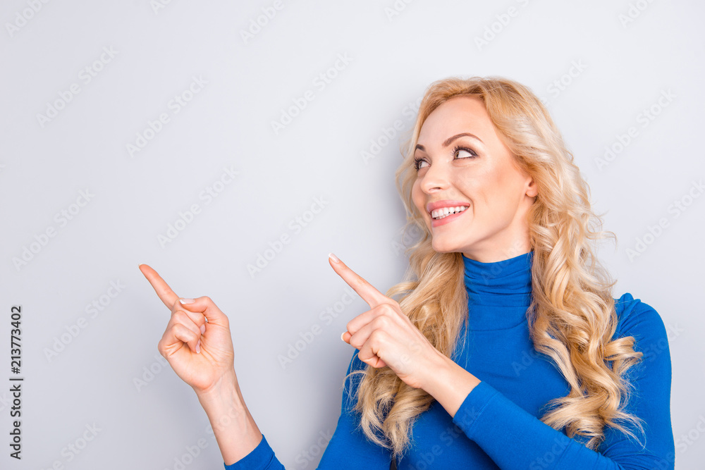 Portrait of stylish, pretty, charming, nice, sexy, cute, blonde woman in blue roll neck pointing two forefingers to copy space isolated on grey background looking at empty place Portrait of stylish, pretty, charming, nice, sexy, cute, blonde woman in blue roll neck pointing two forefingers to copy space isolated on grey background looking at empty place