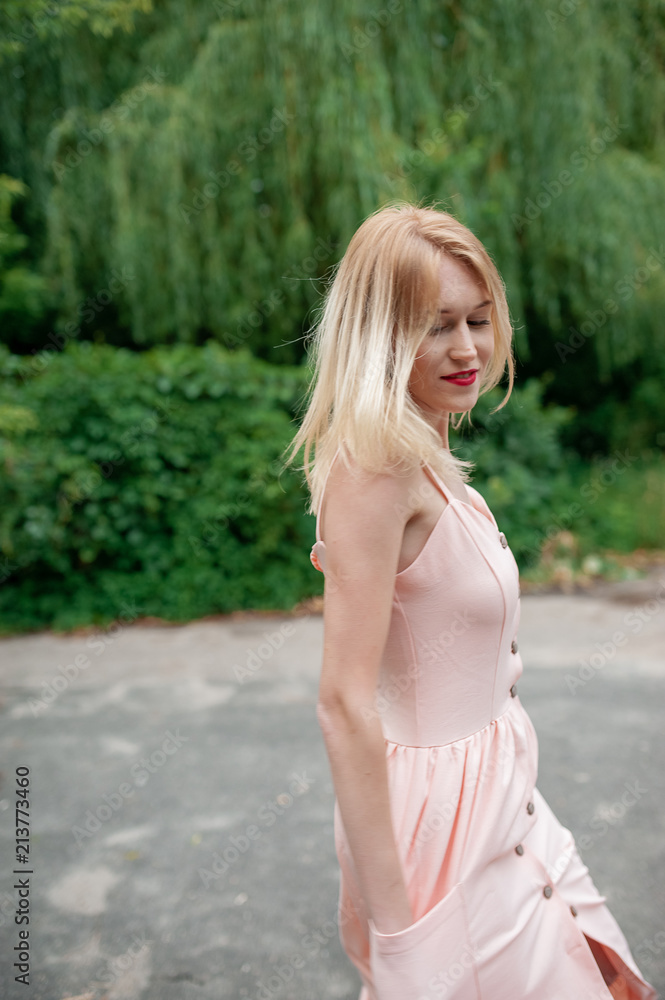 Blondie woman in pink dress in summer forest. Young stylish pretty girl dancing and have fan outdoor, have a good time in park on vacations. Natural, beauty, happiness concept Blondie woman in pink dress in summer forest. Young stylish pretty girl dancing and have fan outdoor, have a good time in park on vacations. Natural, beauty, happiness concept